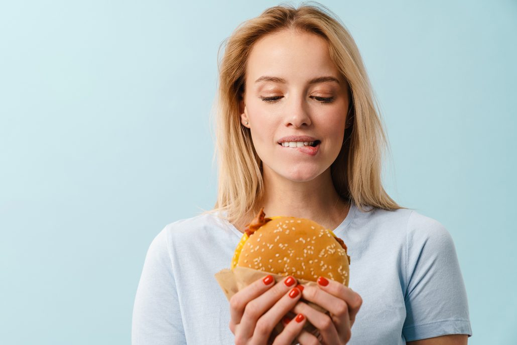 υπάρχει μια γυναίκα που κρατάει ένα burger, το κοιτάει και δαγκώνει τα χείλη της