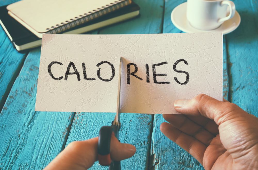 υπάρχει ένα λευκό χαρτόνι που γράφει calories και δύο χέρια με ενα ψαλίδι που το κόβουν στη μέση.